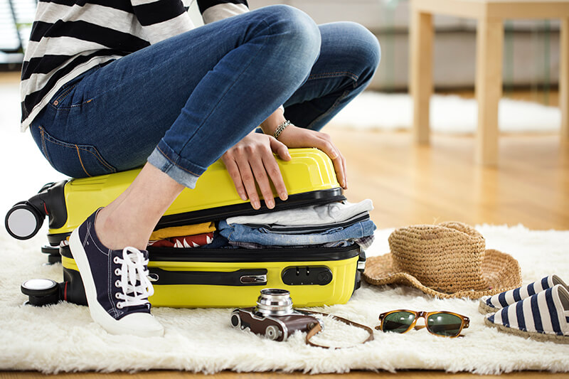 Female squeezing items into a suitcase