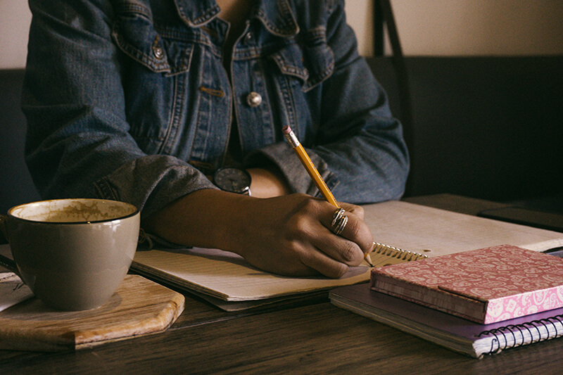 Female student writing in a notebook with a stack of books