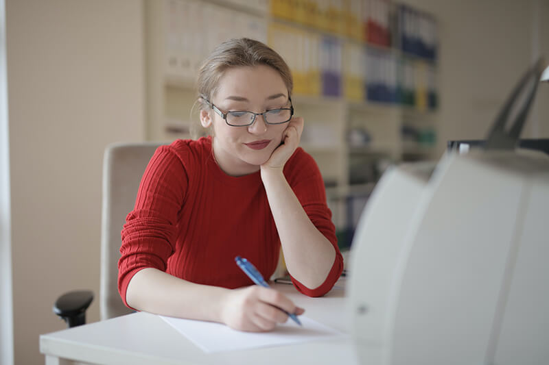 Female student writing at a desk in a red shirt