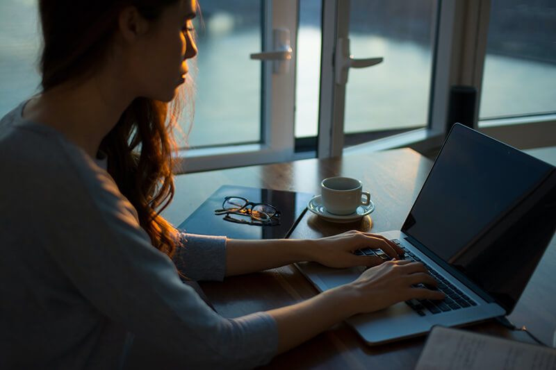 Female student writing a paper using her laptop on a desk