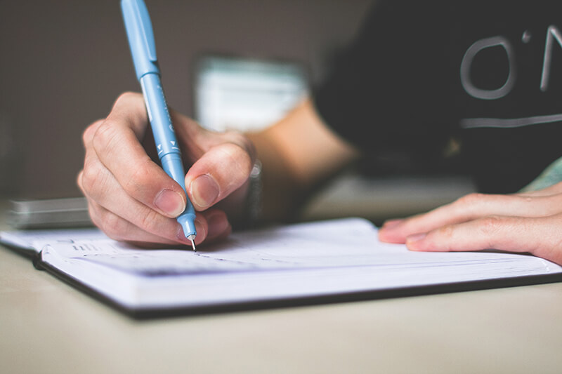 College student writing the first draft of an analytical essay in a notebook