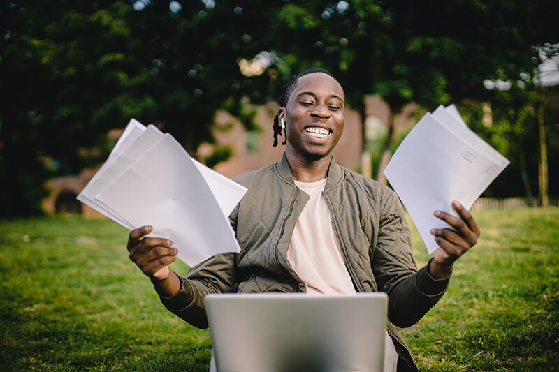 College student happily looking through research topics on his laptop