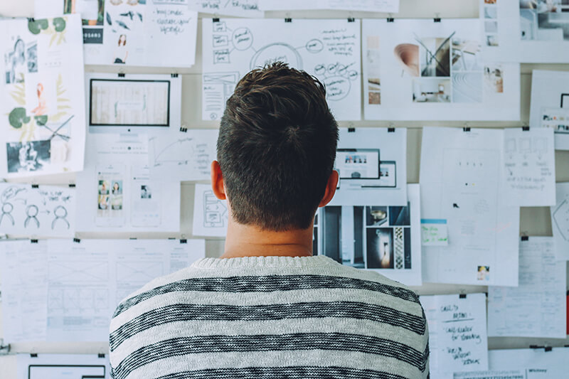 Young man facing a wall of papers looking for topic ideas