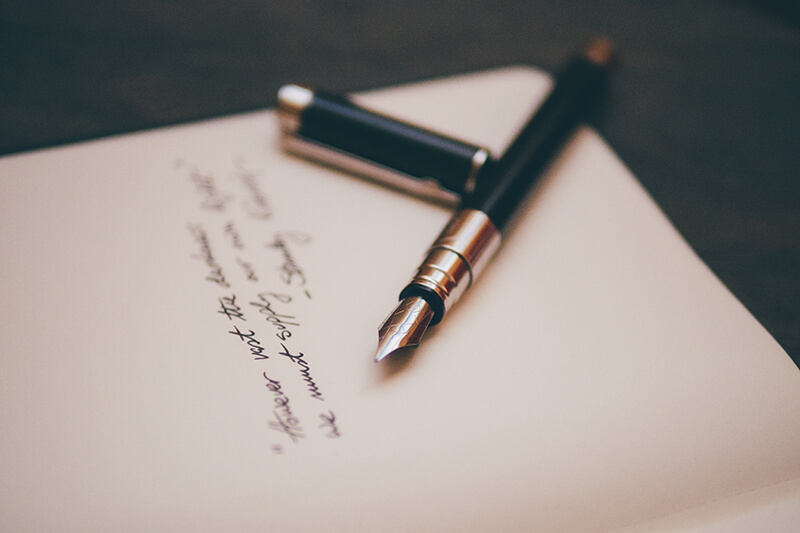 Closeup of fountain pen on a notepad writing different types of sentences