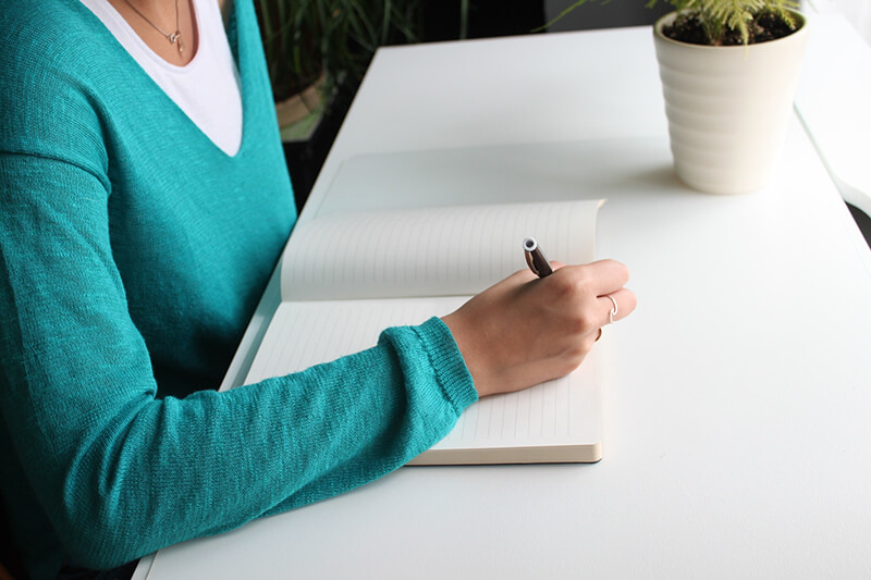 College female sitting at her desk with pen and paper writing an essay