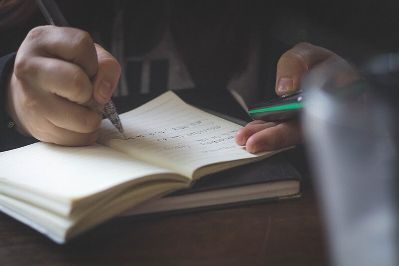 Closeup of student with a pen and smartphone writing a reflection paper