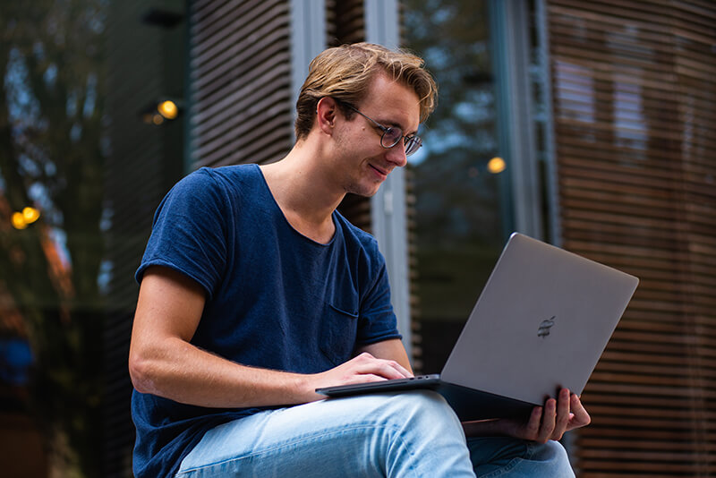 College student sitting outside and going over his essay on his laptop