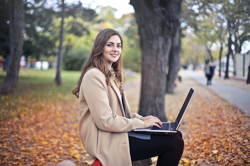 College student using her laptop in a park to develop her essay structure