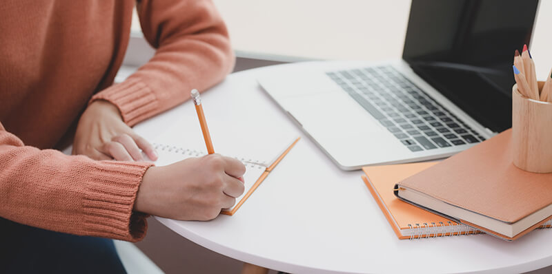 Female student writing a paper at her desk with closeup of her arm