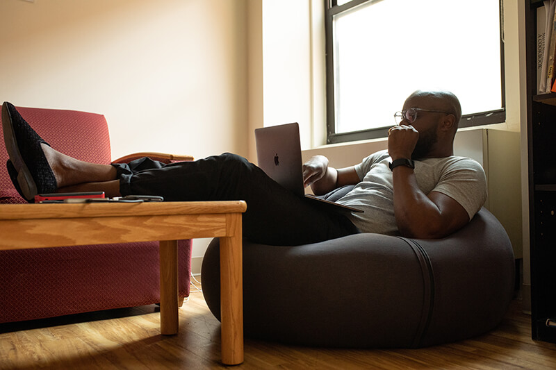 Male college student working on a thesis from a bean bag chair