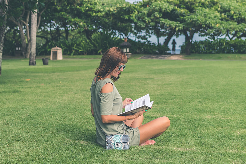 Female college student sitting outside reading a book in the sun