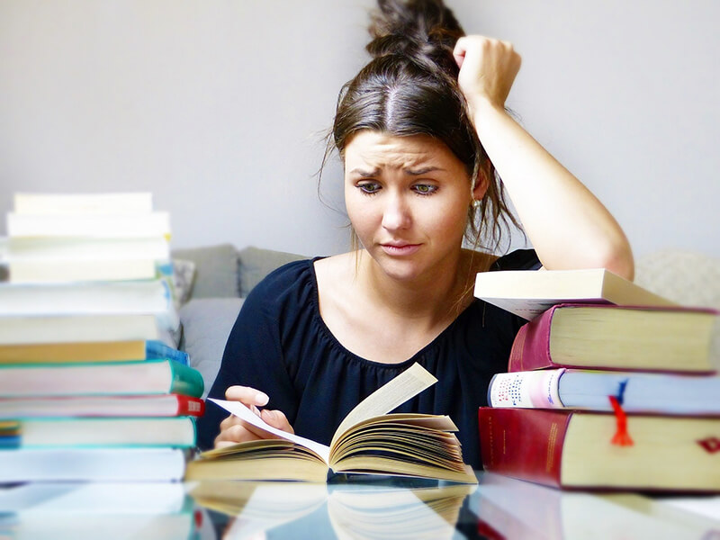Female student confused while trying to analyze a pile of books