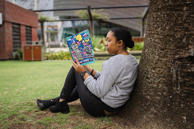 College student sitting outside reading a book to analyze