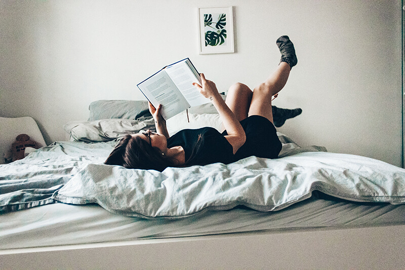 College student laying in her dorm room reading a book for her character analysis essay