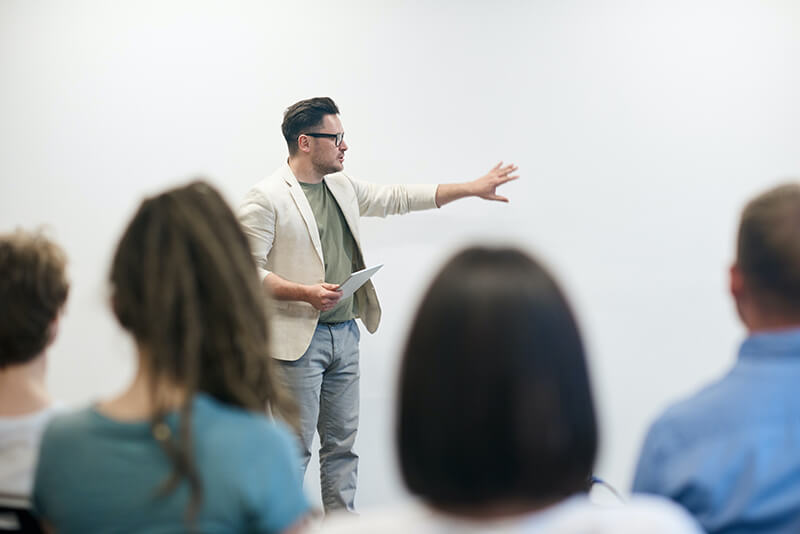 Man wearing a blazer presenting a lesson to a group of students