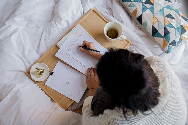 Female writing in a notebook while laying on her bed