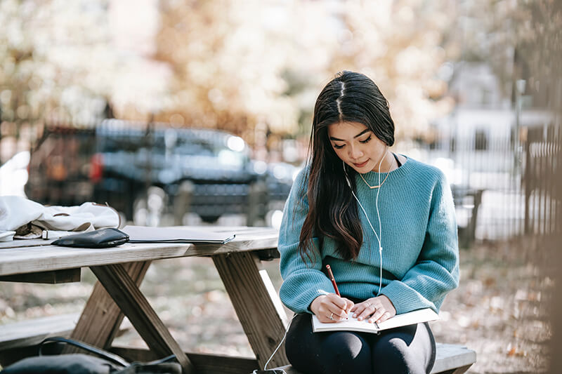 Female college student writing her essay on note paper with a pen