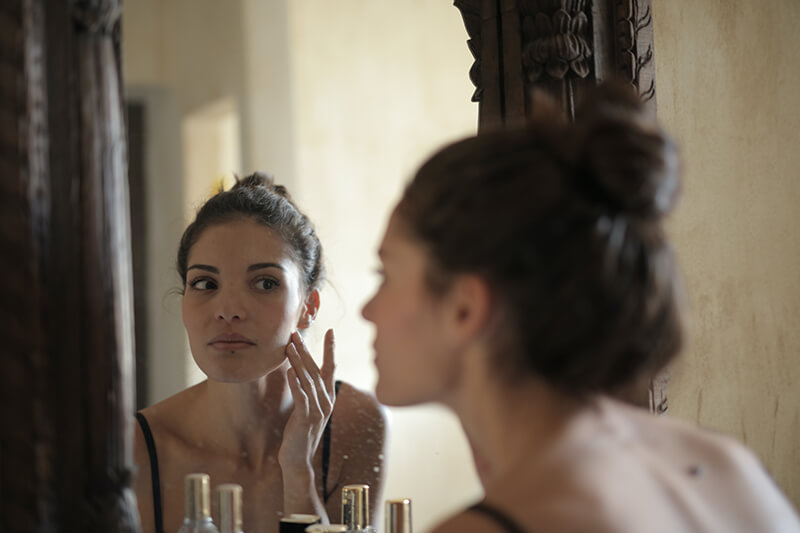 Young woman using some beauty self care ideas in the bathroom mirror