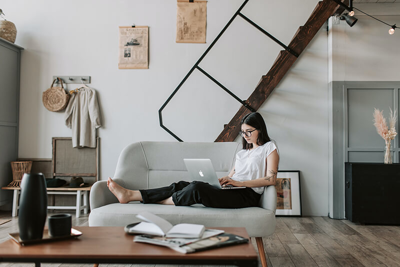 Female college student writing a paper on a laptop on her couch