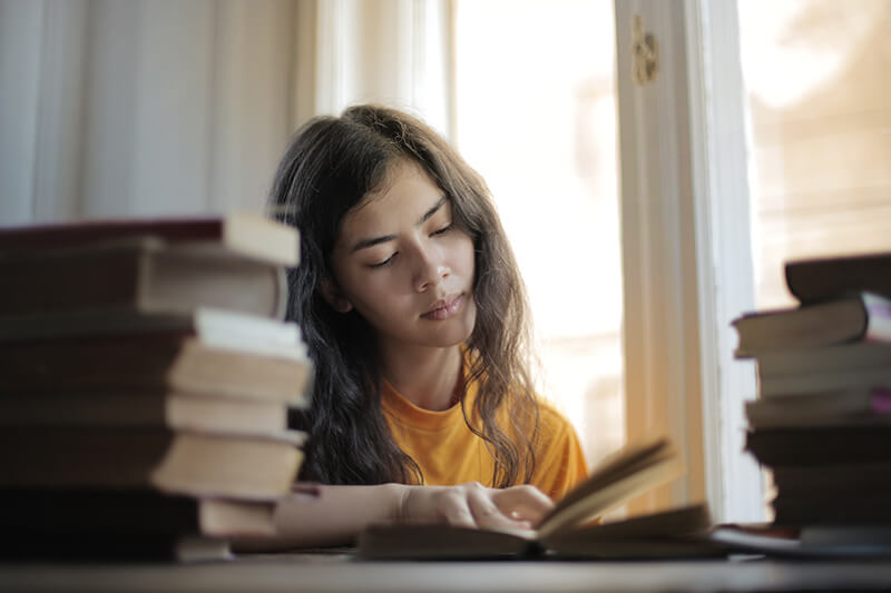 Woman in yellow shirt reading through a stack of books for research in a literature review