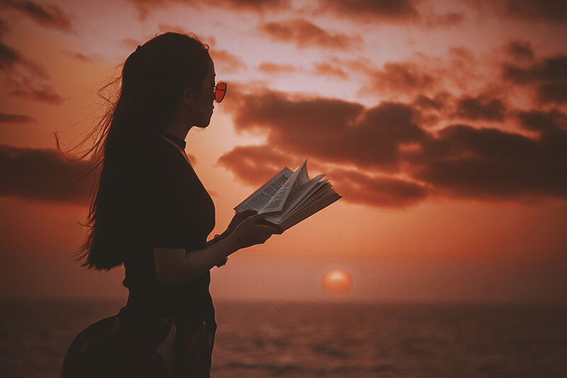 Young woman standing in front of a sunset with literature in a book
