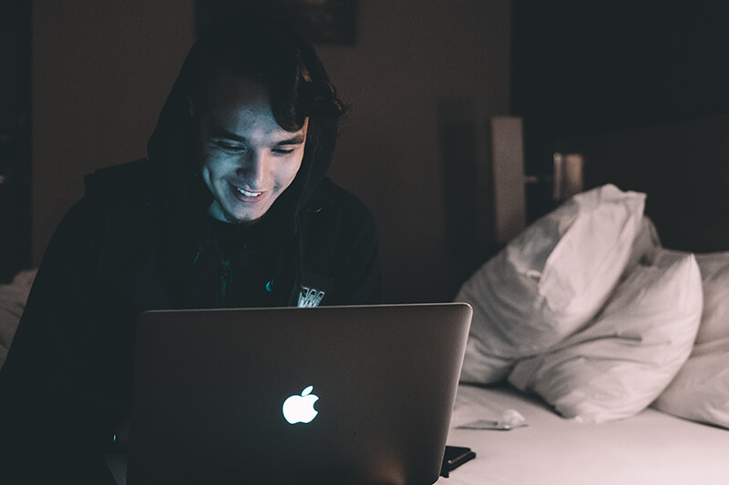 Male student sitting in a college dorm doing homework on a laptop