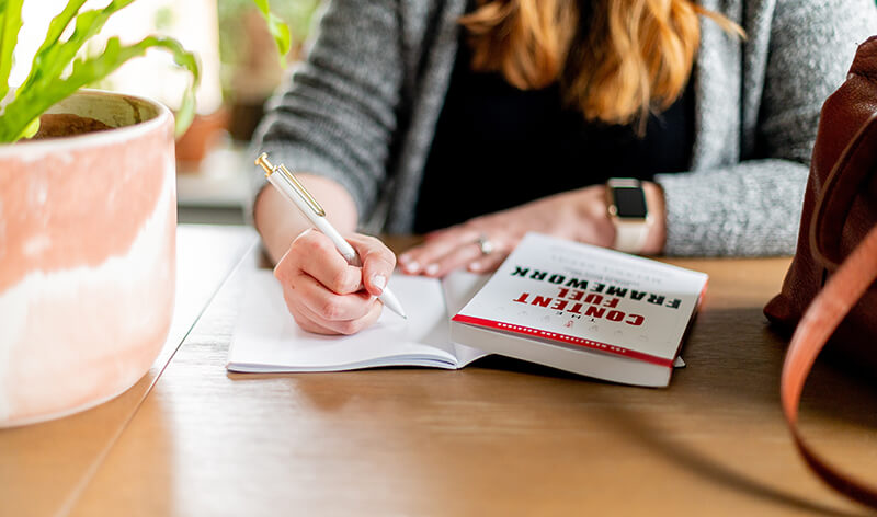 Female student using a textbook and notepad to record notes from a lecture