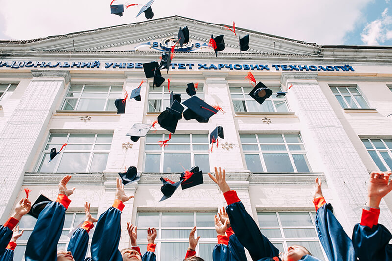 Greek alumni at graduation throwing their caps in the air to celebrate