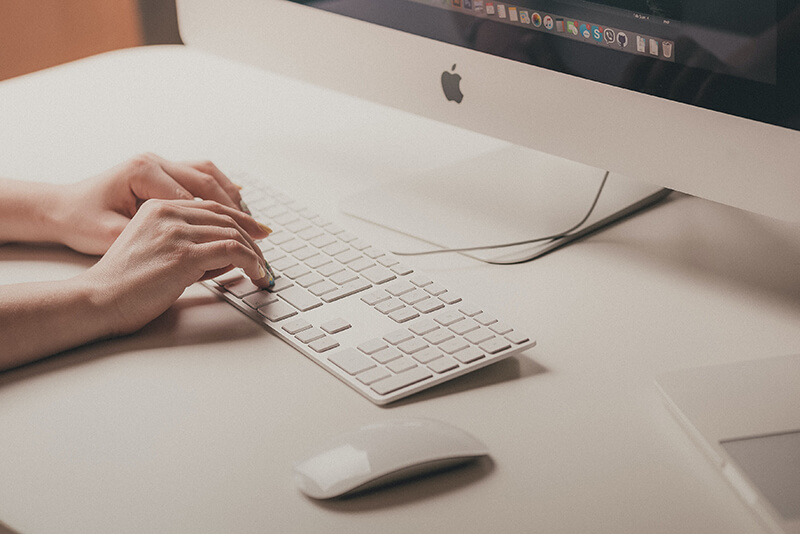 White tone image of hands typing out an expository essay on a mac keyboard