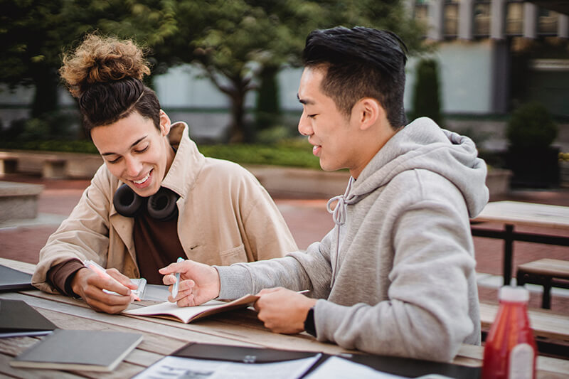 A pair of male college students sitting outside helping each other write an expository essay