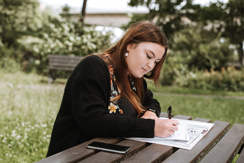 Female student writing an expository essay at a table outside