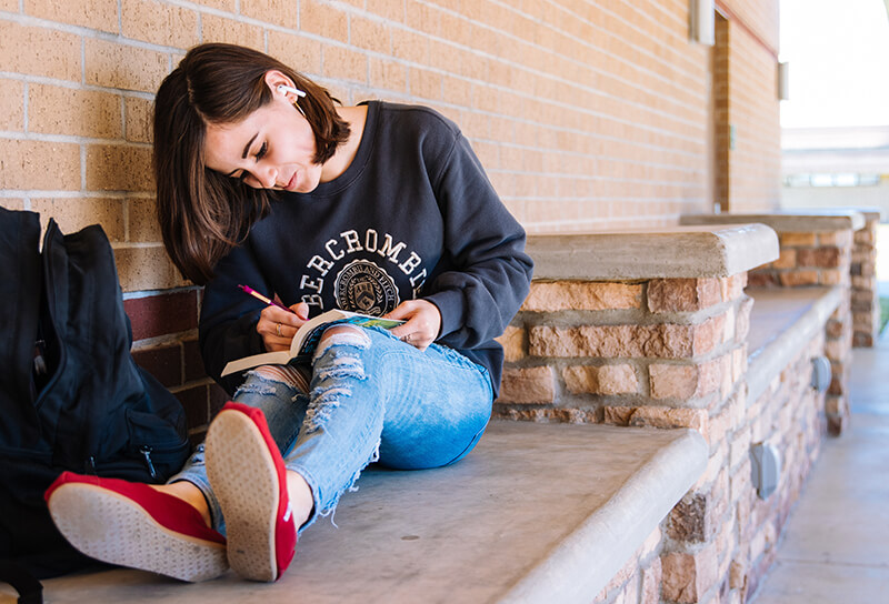 Female college student sitting on a step doing her essay writing outside