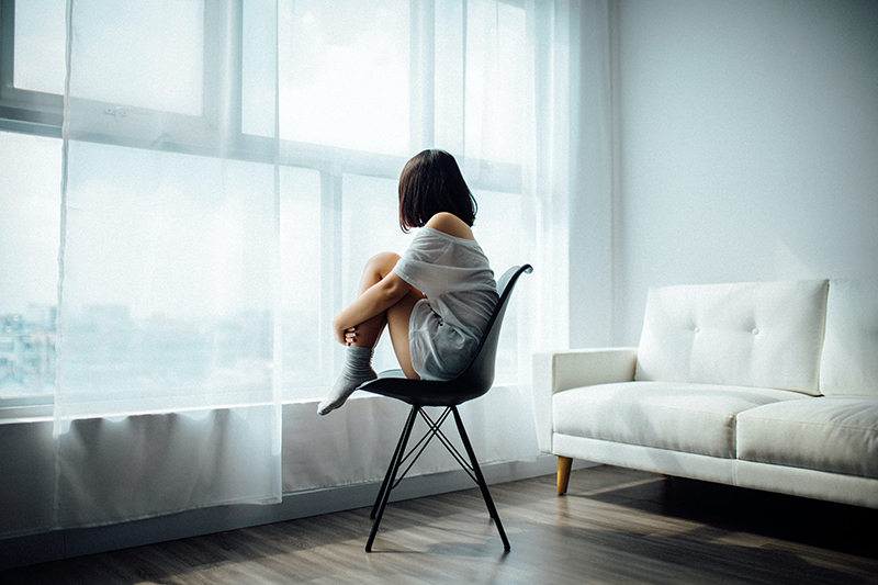 Homesick female student sitting on a chair alone in front of the window