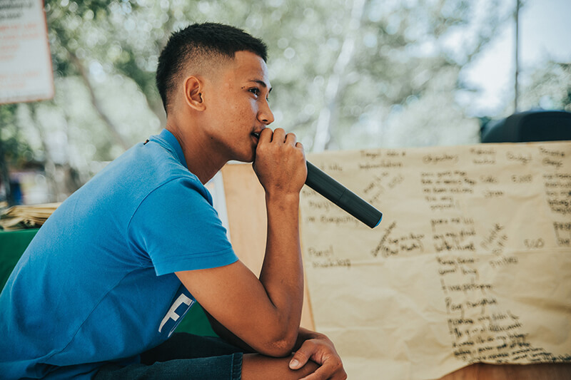 Male college student in a blue shirt making a persuasive speech into a microphone