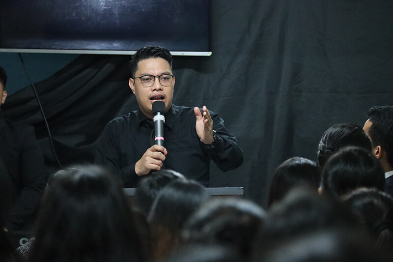 Young man making a speech into a microphone in front of a class