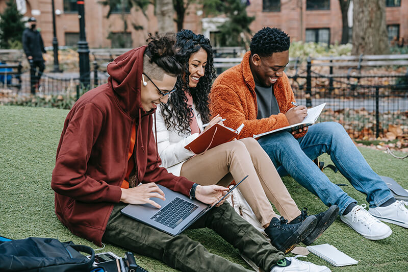 Group of students helping each other with college essays at school outside