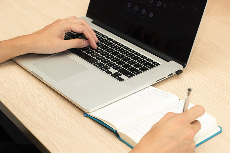 a student taking notes on paper and on his laptop