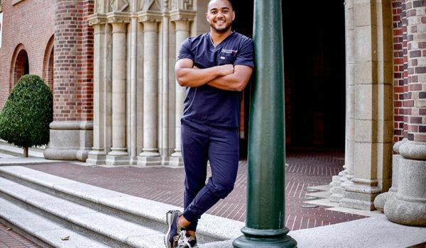 Levi Powell wearing scrubs and smiling proudly in front of dental school