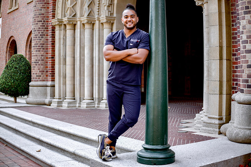 Levi Powell wearing scrubs and smiling proudly in front of dental school