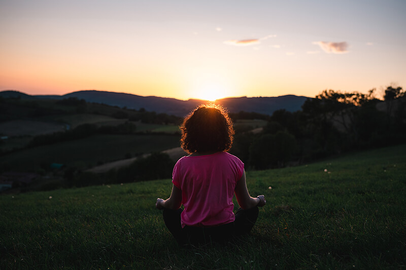 woman meditates in a field while trying to regain motivation